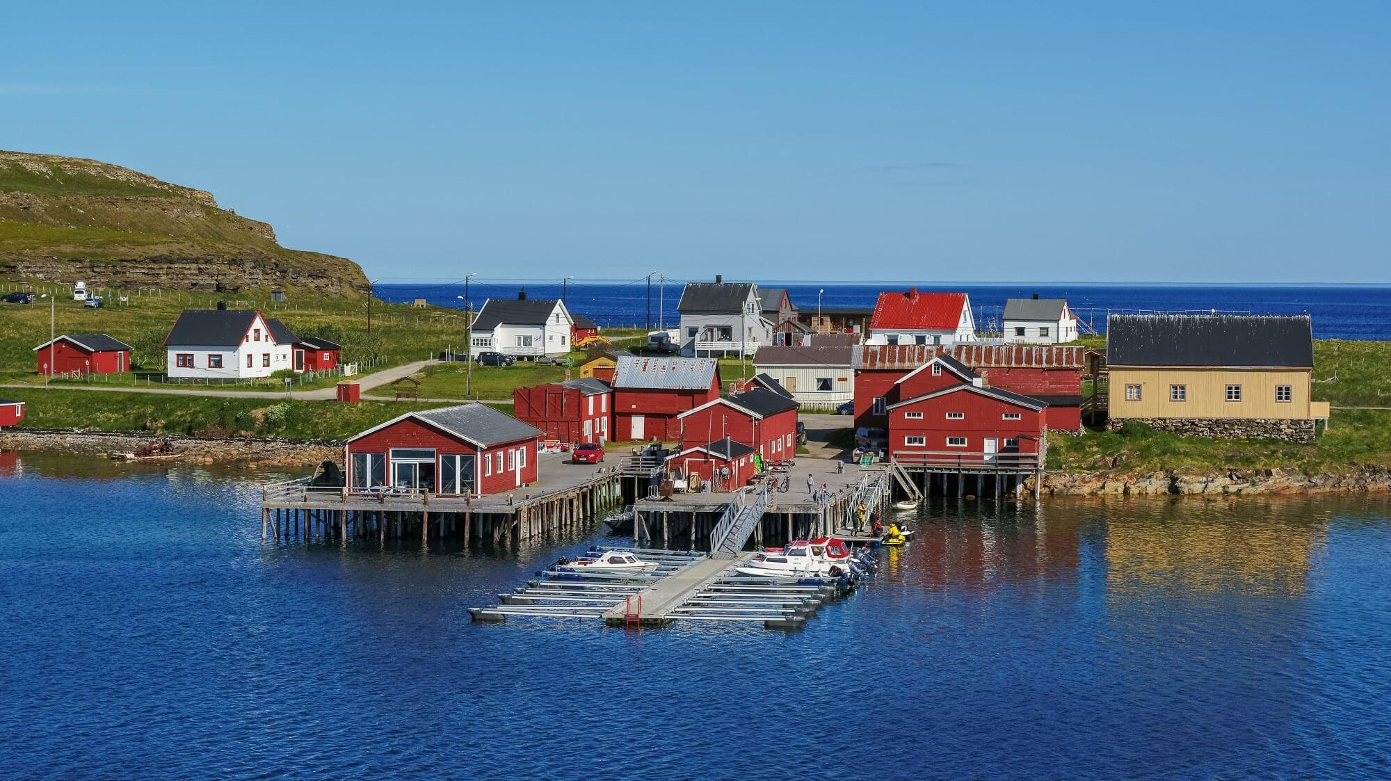 Røde rorbuer og brygge på Ekkerøy med blått hav og klart vær